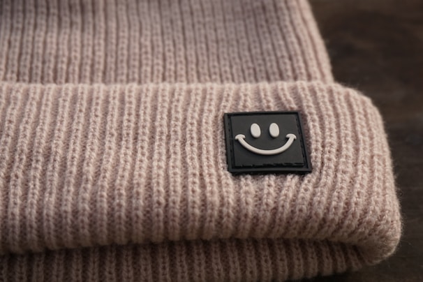 Close-up of apeace logo embroidered on a black beanie with a blurred city background.