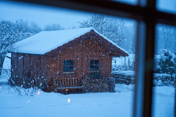 A cozy fireside moment inside a forest cabin in Kashmir, with snow falling gently outside.