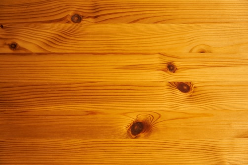 The image features a close-up view of wooden planks with a natural grain pattern. The wood has a smooth finish, with distinct knots and lines that create a unique texture.