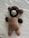 A handmade crocheted bear is lying on a smooth, white surface. It has a brown body, darker brown arms and head, lighter brown ears, and a cream-colored muzzle. The bear features black eyes and an expressionless face.