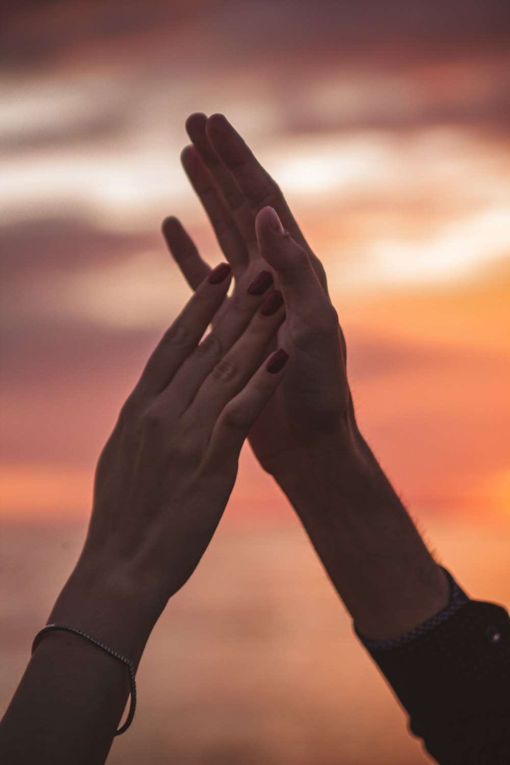 two hands reaching up into the air with a sunset in the background
