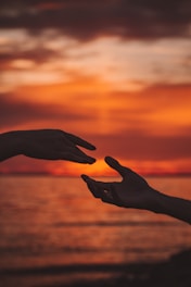 two hands reaching out towards each other in front of a sunset