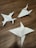 Three paper origami models resembling shurikens are placed on a wooden surface. The models are crafted from white paper, showcasing precise folds and pointed edges. A small mark or writing is visible on one of the models.