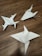 Three paper origami models resembling shurikens are placed on a wooden surface. The models are crafted from white paper, showcasing precise folds and pointed edges. A small mark or writing is visible on one of the models.