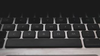 Close-up view of a black computer keyboard with visible keys for letters, arranged in a standard QWERTY layout. The lighting is dim, creating a slightly moody or somber atmosphere.