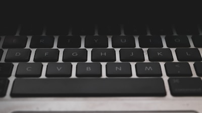 Close-up view of a black computer keyboard with visible keys for letters, arranged in a standard QWERTY layout. The lighting is dim, creating a slightly moody or somber atmosphere.