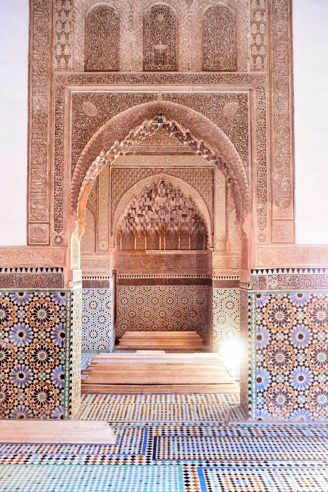 An ornate carved stucco mihrab niche above a zellige-tiled chamber in the Saadian Tombs.