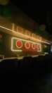 A cozy interior with a long counter lined with stools. A neon sign with Chinese characters and the text 'Little Hong Kong' glows above the counter. The room is dimly lit, adding to a warm and inviting atmosphere, with colorful balloons visible in the background.