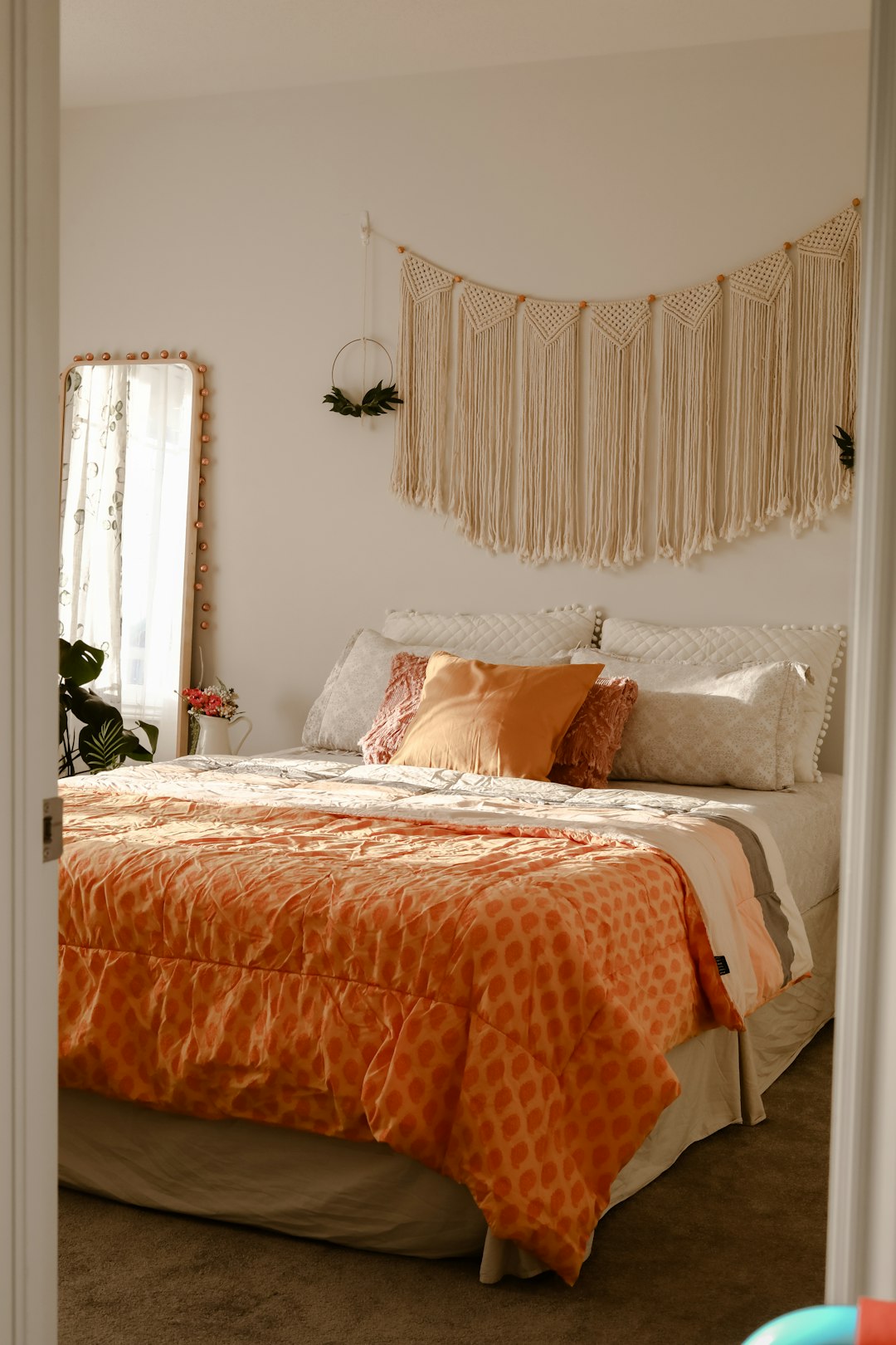 Bed with rust colored bedding under a macrame wall hanging
