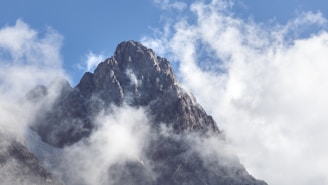 A mountain peak piercing through clouds under a clear blue sky.