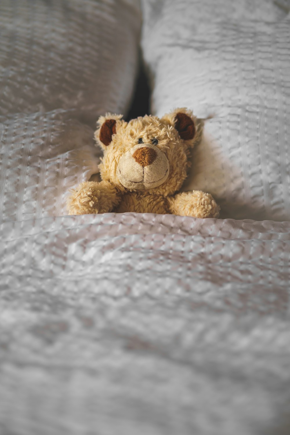 a teddy bear laying on a bed with white sheets