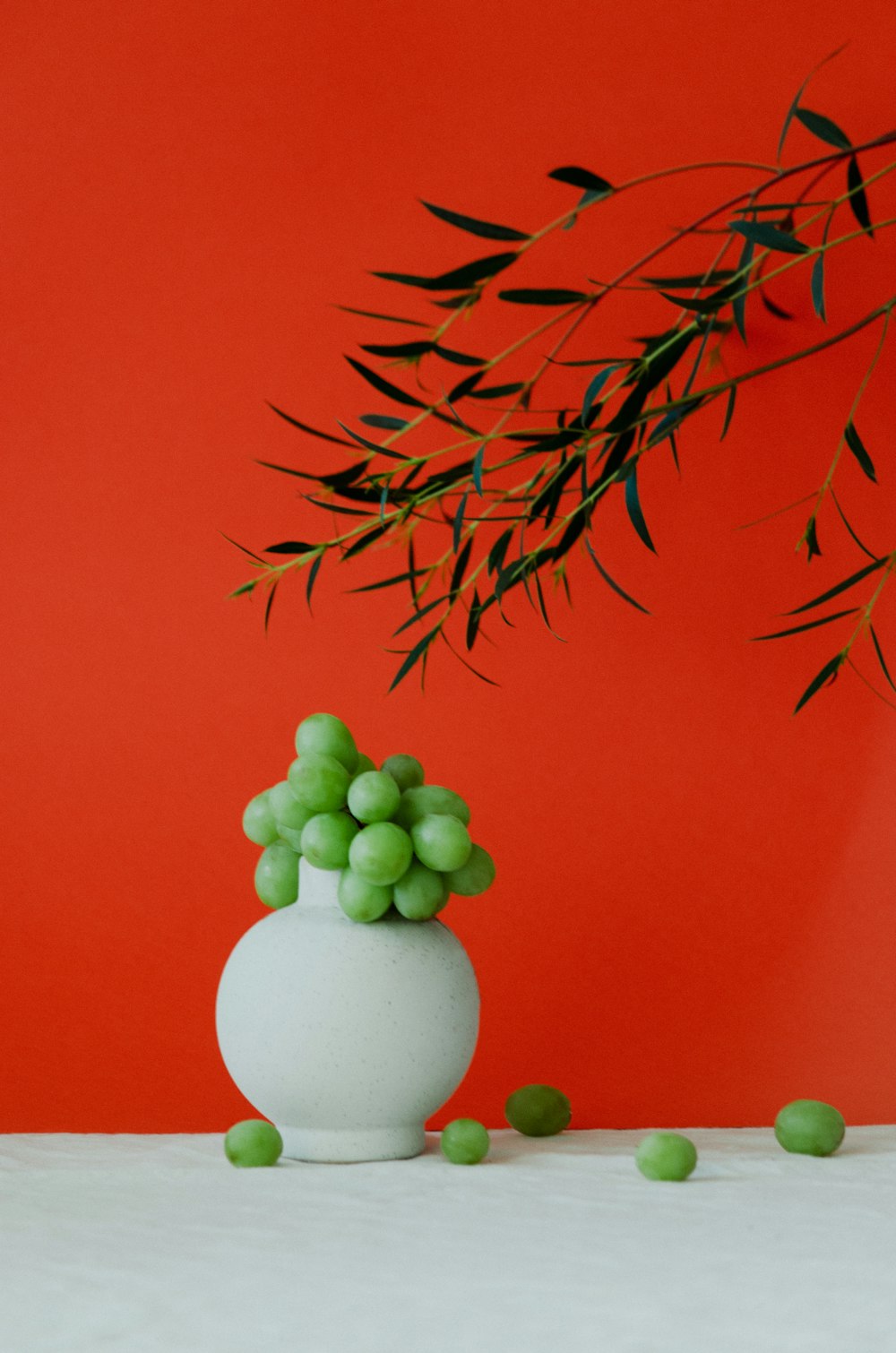 a white vase filled with green grapes on top of a table