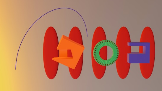 A series of abstract geometric shapes are arranged on a flat surface. There are elongated red ovals placed horizontally, alongside an orange angular shape resembling a house, a green circular gear, and a purple rectangular block. A purple curve arcs over the composition from left to right. The background transitions from dark yellow on the left to beige on the right.