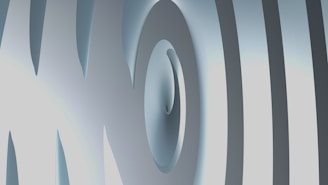 An abstract 3D design featuring curved and overlapping smooth surfaces. The image has a metallic-like texture with varying shades of gray and hints of light blue.