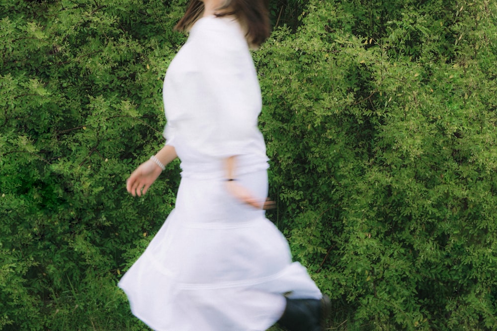 a woman in a white dress is walking by some bushes