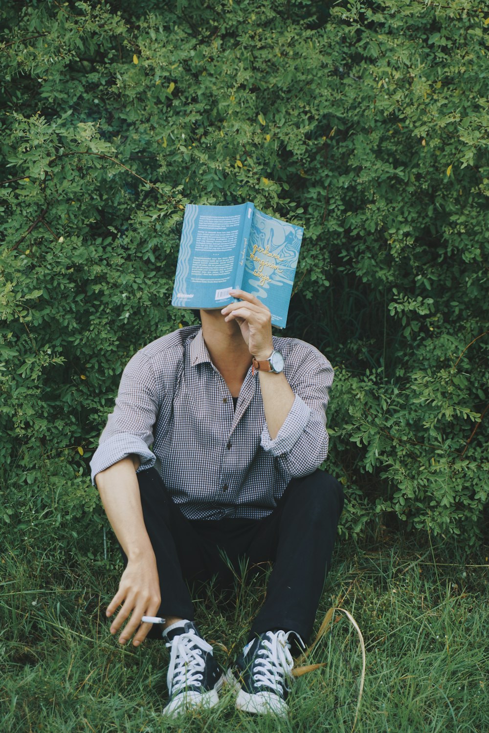 a man sitting in the grass with a book on his head