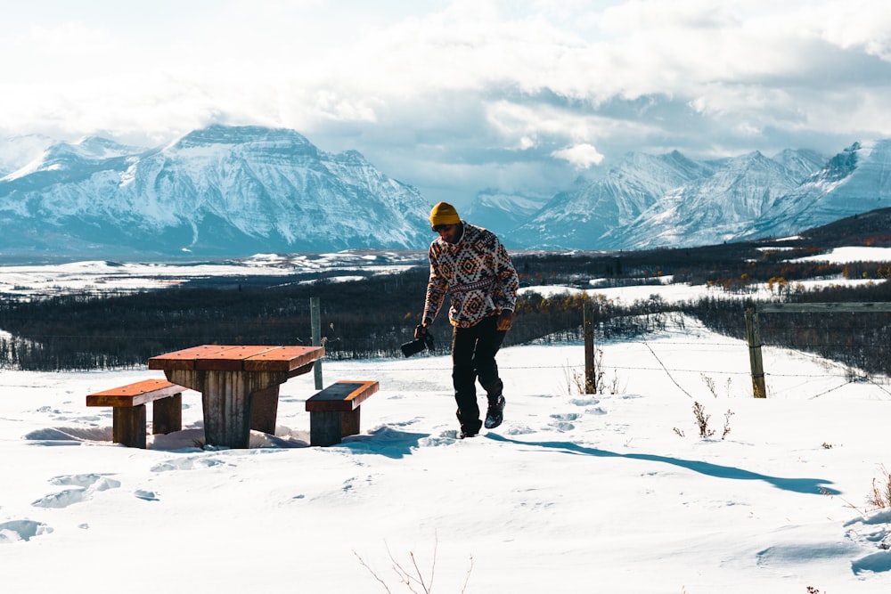 a man standing in the snow next to a picnic table