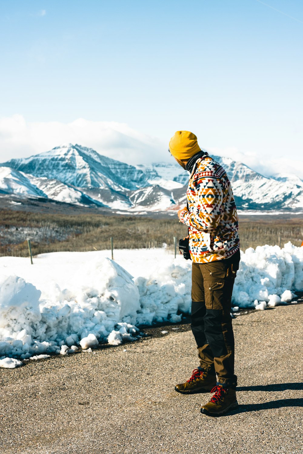 a man standing on a road in front of snow covered mountains