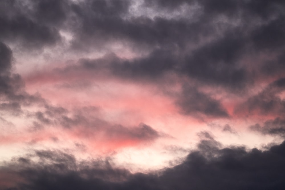 a plane flying through a cloudy sky at sunset