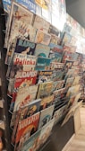 A collection of vintage-style metal signs displayed on a rack. The signs feature various themes, including advertisements, classic imagery, and slogans, with references to Budapest and retro designs.