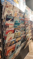 A collection of vintage-style metal signs displayed on a rack. The signs feature various themes, including advertisements, classic imagery, and slogans, with references to Budapest and retro designs.