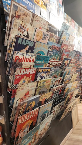 A collection of vintage-style metal signs displayed on a rack. The signs feature various themes, including advertisements, classic imagery, and slogans, with references to Budapest and retro designs.