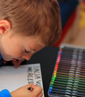 a little boy that is sitting at a table with some crayons