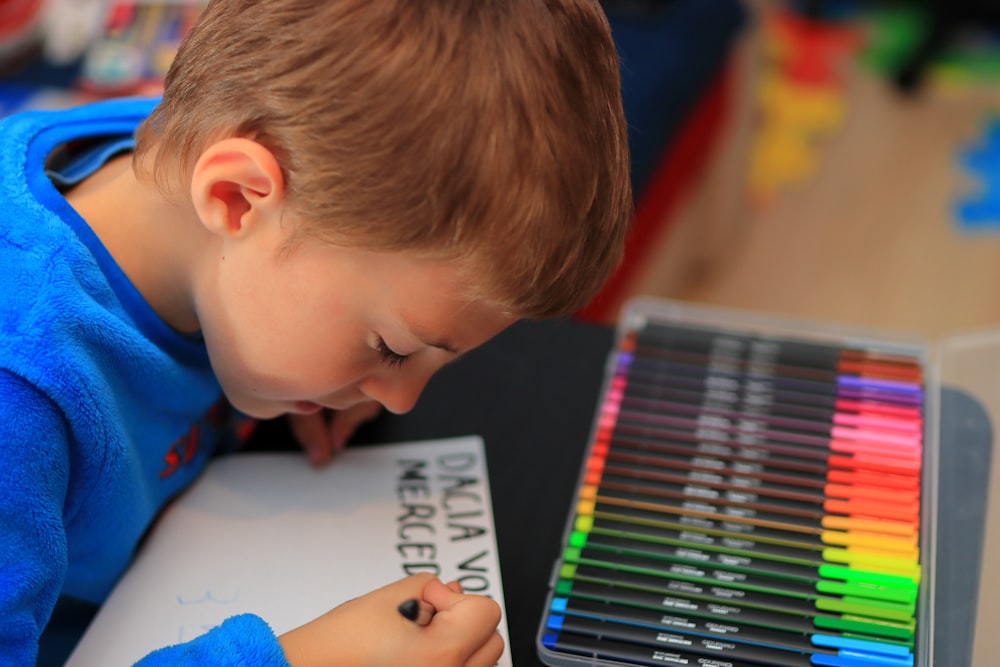 un petit garçon assis à une table avec des crayons