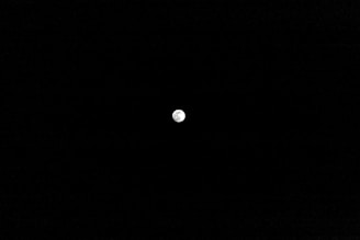 A small, illuminated moon is centered against a vast, dark sky, highlighting its surface features.