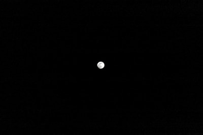 A small, illuminated moon is centered against a vast, dark sky, highlighting its surface features.