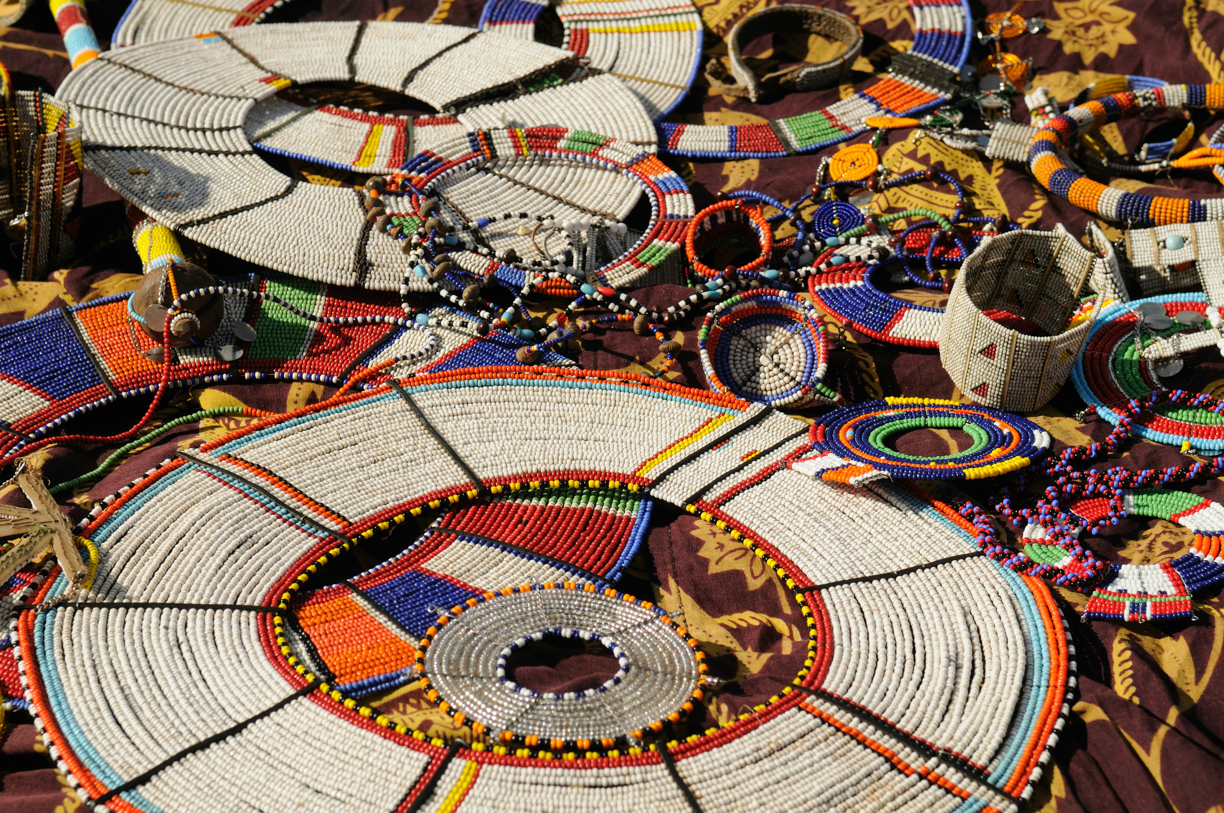 Traditional beaded necklaces and bracelets arranged on patterned fabric.