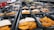 Rows of black meal prep containers are filled with cooked sweet potatoes and slices of turkey, arranged neatly. The containers are placed on a large surface in what appears to be a commercial kitchen setting.