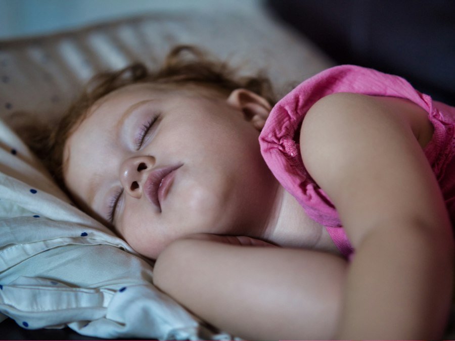 A tired parent standing over a crib at night
