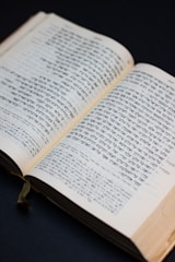 A book is open to display columns of text written in Hebrew script. The pages are slightly yellowed, indicating age or frequent use. A dark background contrasts with the lighter pages, and a green ribbon bookmark is visible along the spine.
