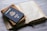 A United States passport is placed on top of a closed leather-bound book, next to an open book with text in a foreign language on a marble surface.