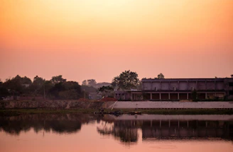A serene lakeside view at sunset with a modern hotel silhouette reflecting on the water.