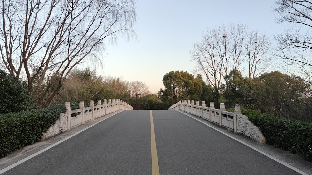 an empty road with a white fence and trees
