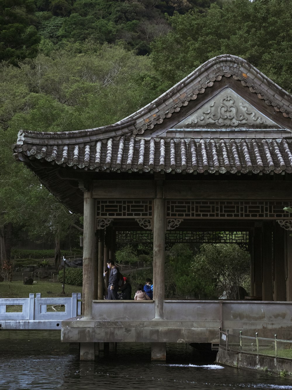 a gazebo with people standing on it next to a body of water