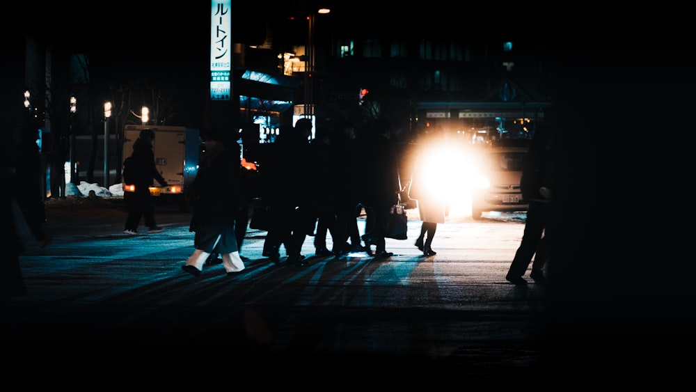 a group of people walking across a street at night