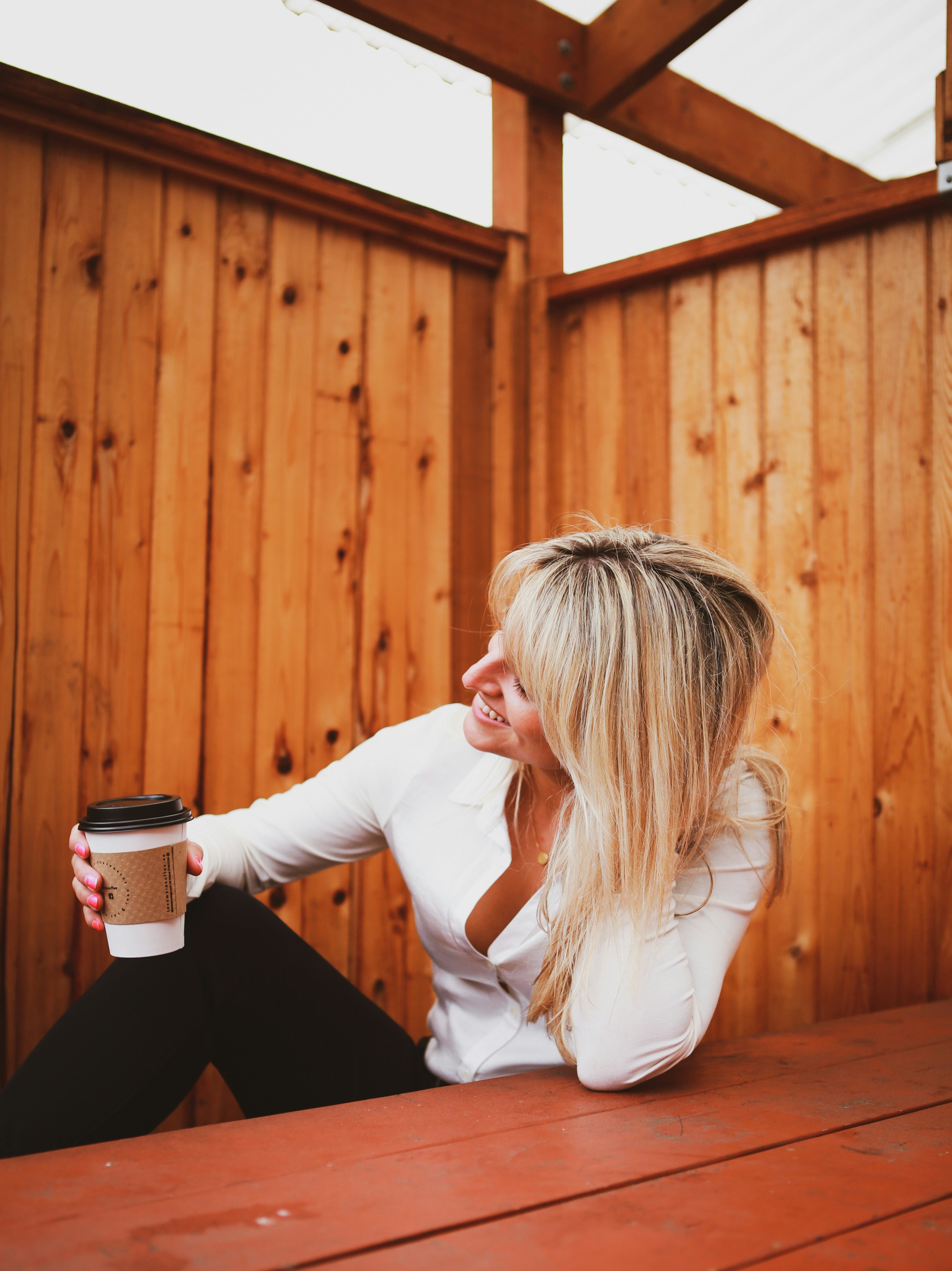 木製のベンチに座ってコーヒーを飲んでいる女性