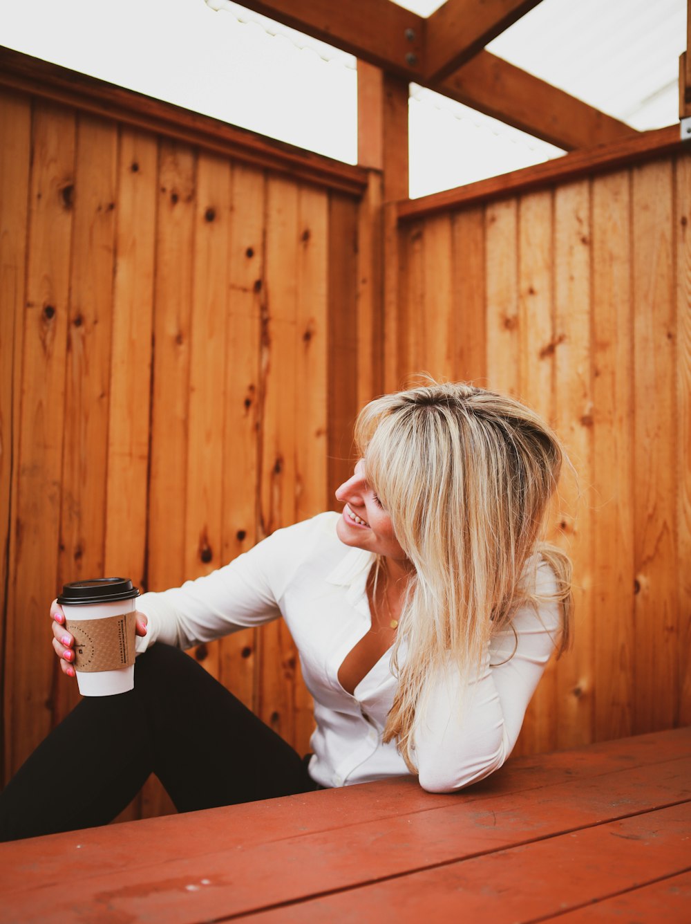 a woman sitting on a wooden bench holding a cup of coffee
