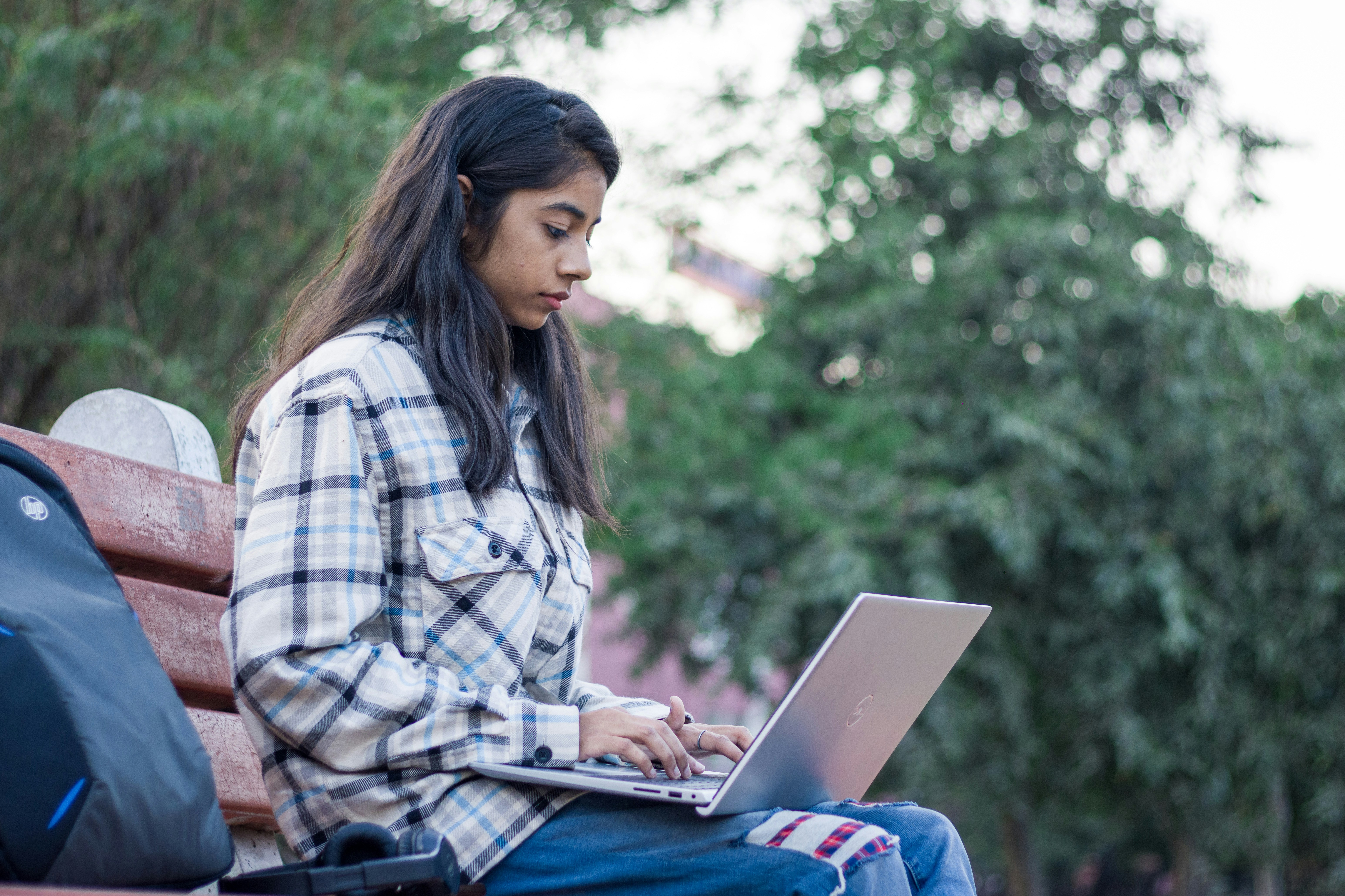 seorang wanita duduk di bangku menggunakan komputer laptop