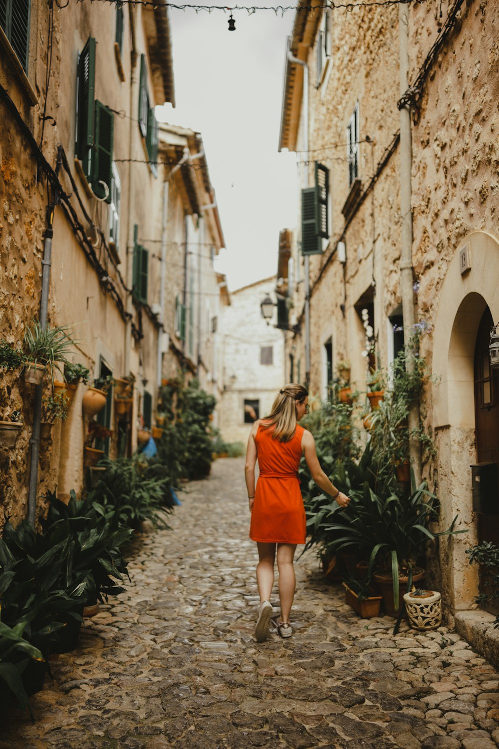 a woman in an orange dress walking down a cobblestone street