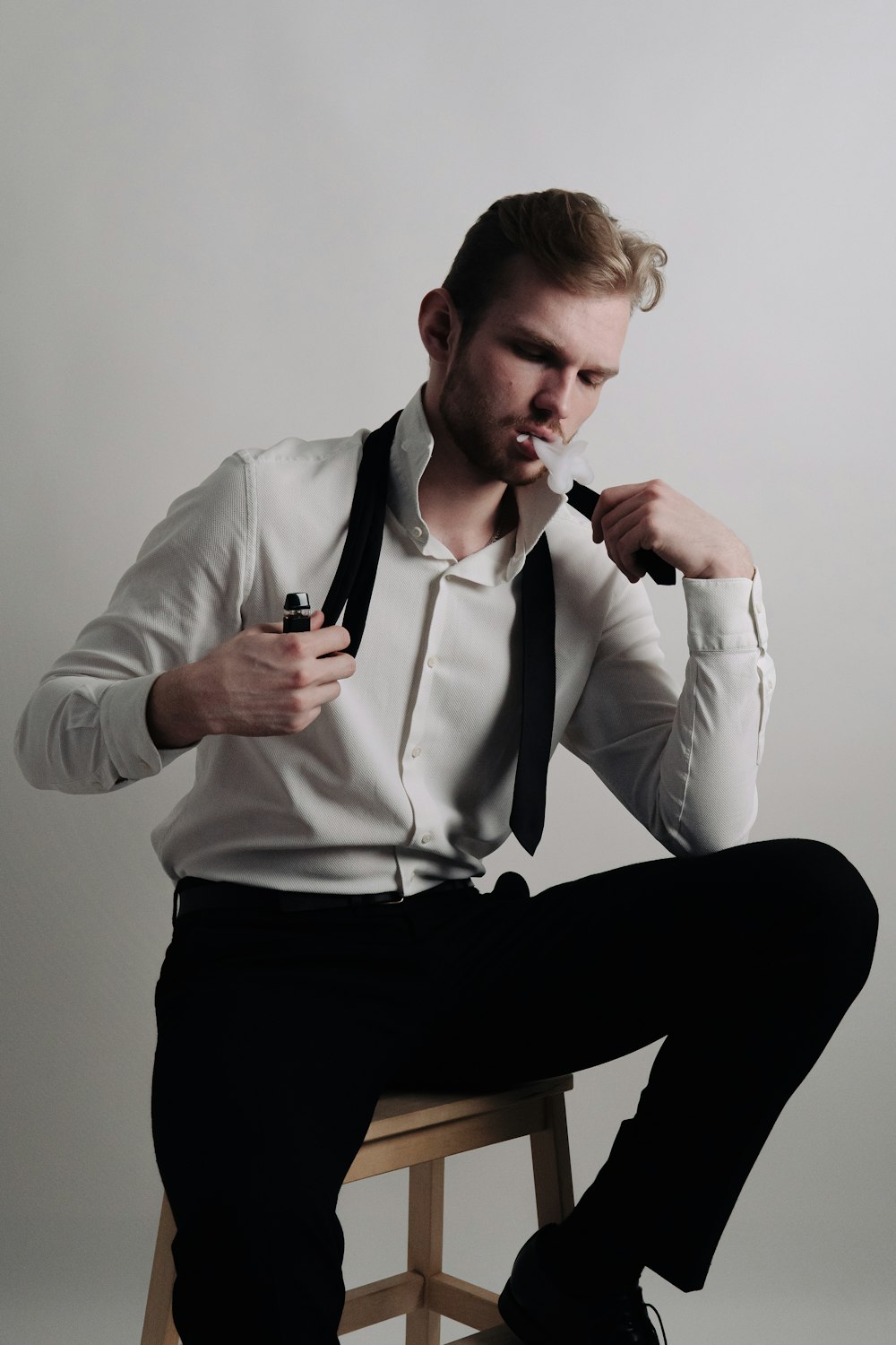 um homem de camisa branca e gravata preta sentado em um banquinho
