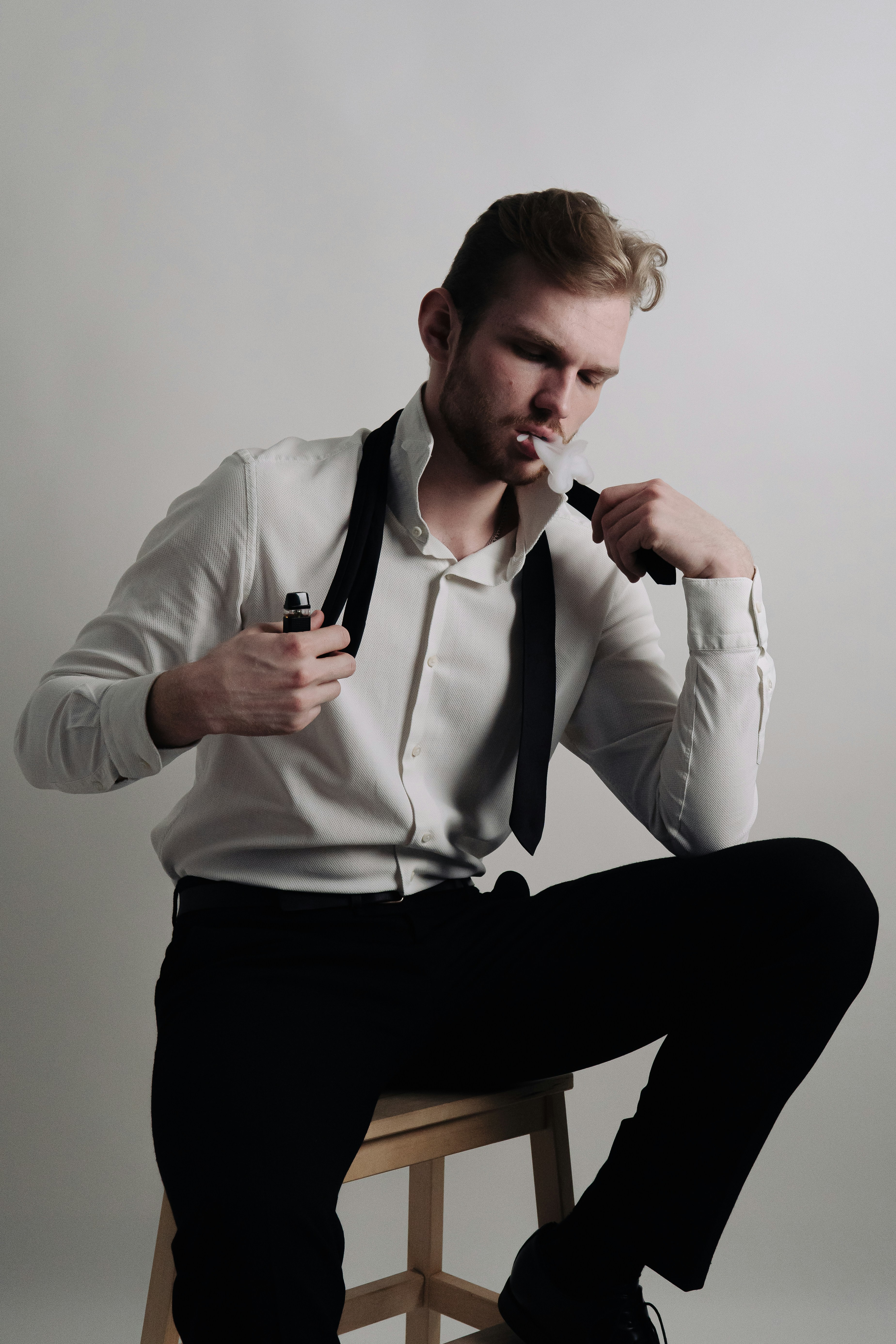 A man in a classic shirt, trousers and shoes sits and smokes thoughtfully