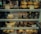 An assortment of baked goods and desserts displayed on shelves, including bread rolls, cakes, tiramisu in glasses, chocolate desserts in dishes, and pastries with labels indicating their names and prices.