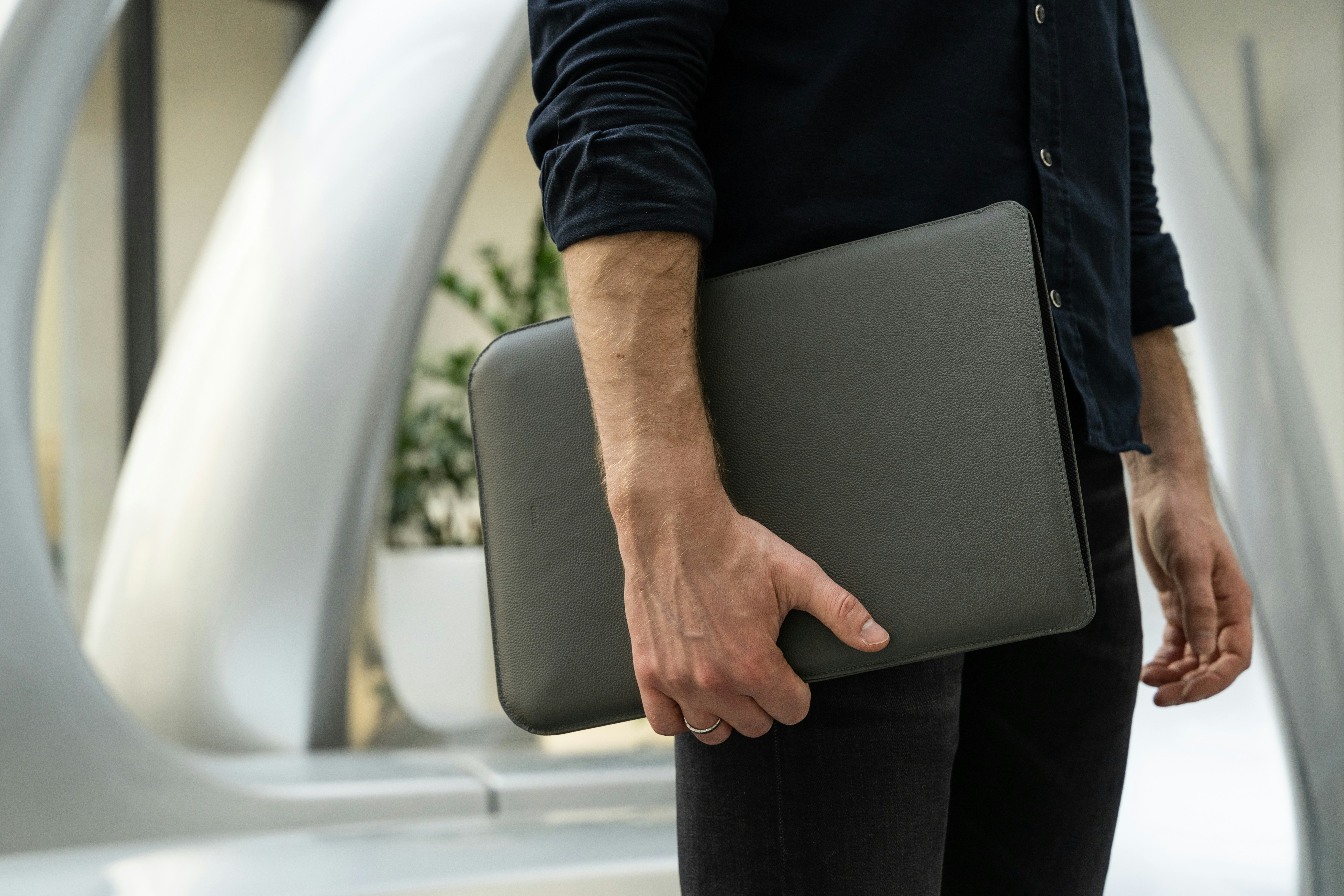 A photo of a man standing with a MacBook in a leather sleeve in his hands