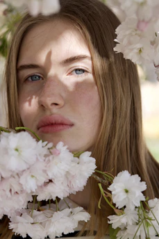 A serene close-up of Kimberly smiling gently, surrounded by soft pink blossoms that reflect her warm, self-loving spirit.