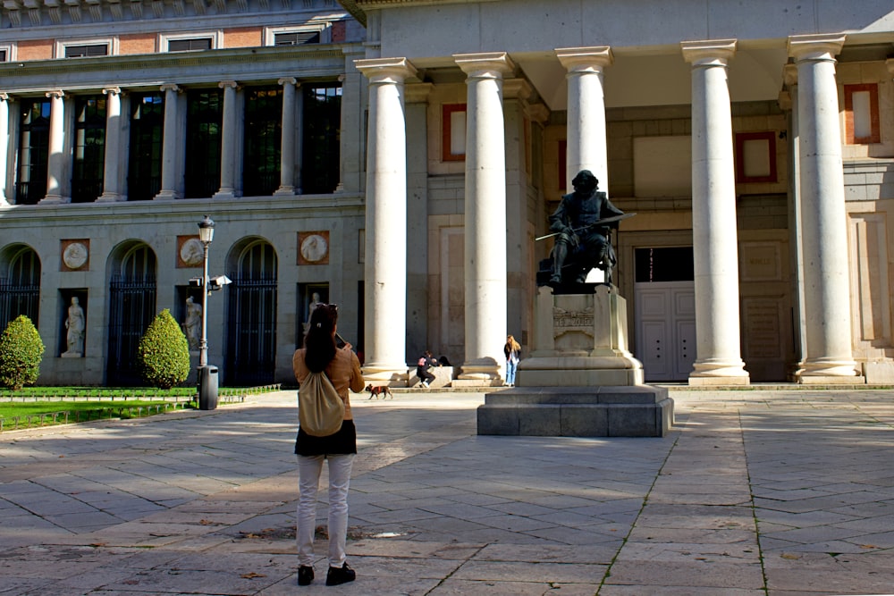 a woman taking a picture of a statue in front of a building