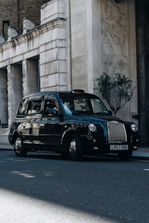 a black taxi cab driving down a street next to a tall building